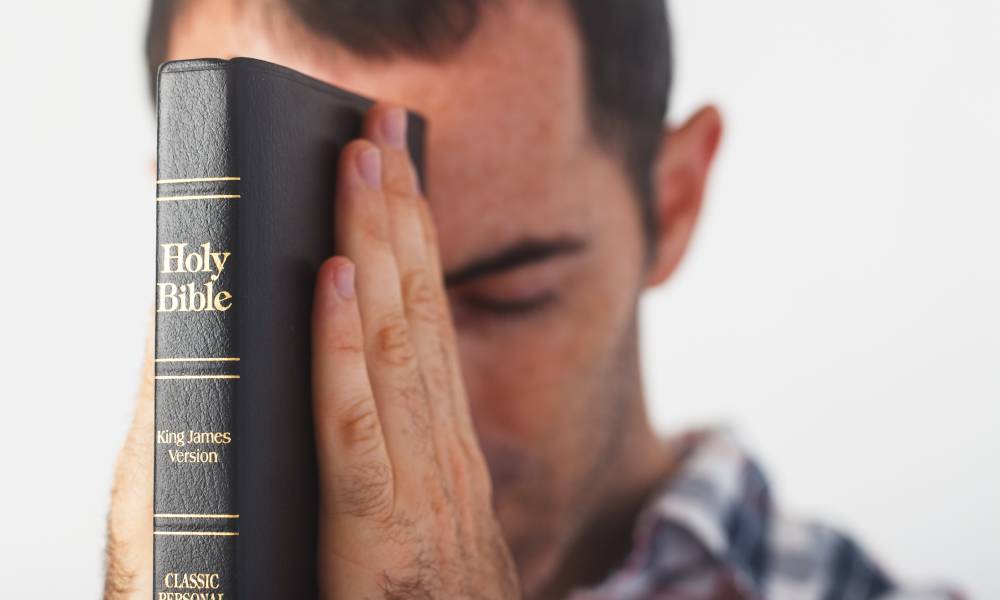 Man praying while holding a King James Bible with the words 'classic personal reference' on the spine to his forehead