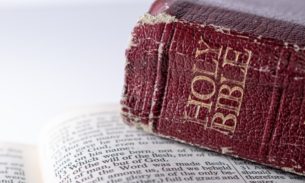 Bible with red binding showing visible wear on the binding sitting on top of another Bible open to John1:13-14