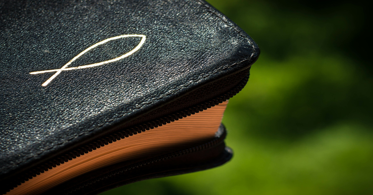 Close-up of a corner of a leather book cover embossed with a Christian fish symbol. The book is closed, and the cover is unzipped.