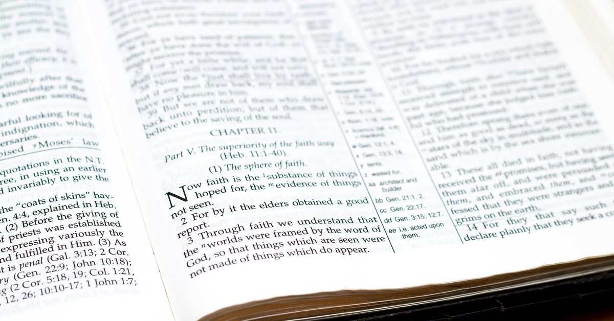 A Bible opened to Hebrews 11:1 resting on a wooden table; its pages are pristine, white, and untorn, with clear text.