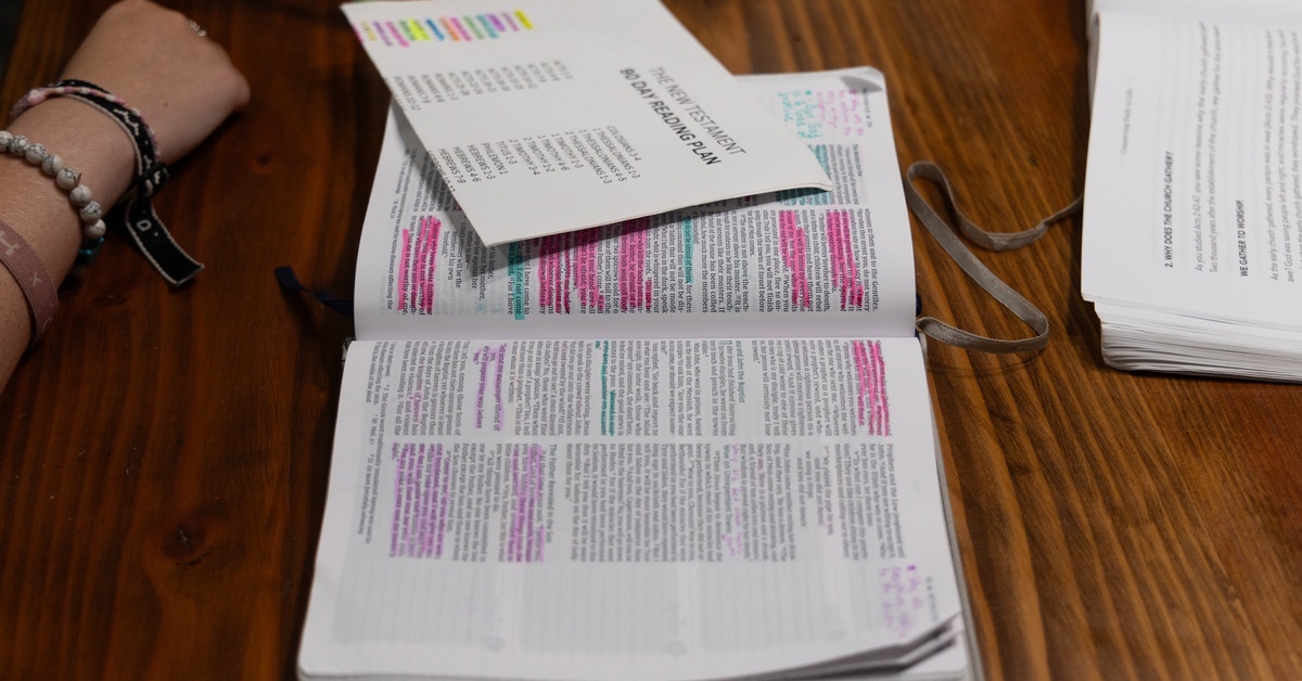 An open Bible with highlighted verses and notes written in its wide margins. A ninety-day reading plan lies on top of it.