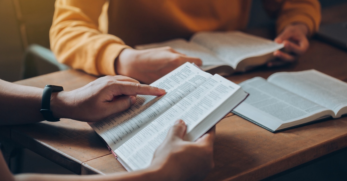 What To Know About Dispensationalist Theology People sitting at a table read their Bibles together. One person points to a verse in their double-column Bible.