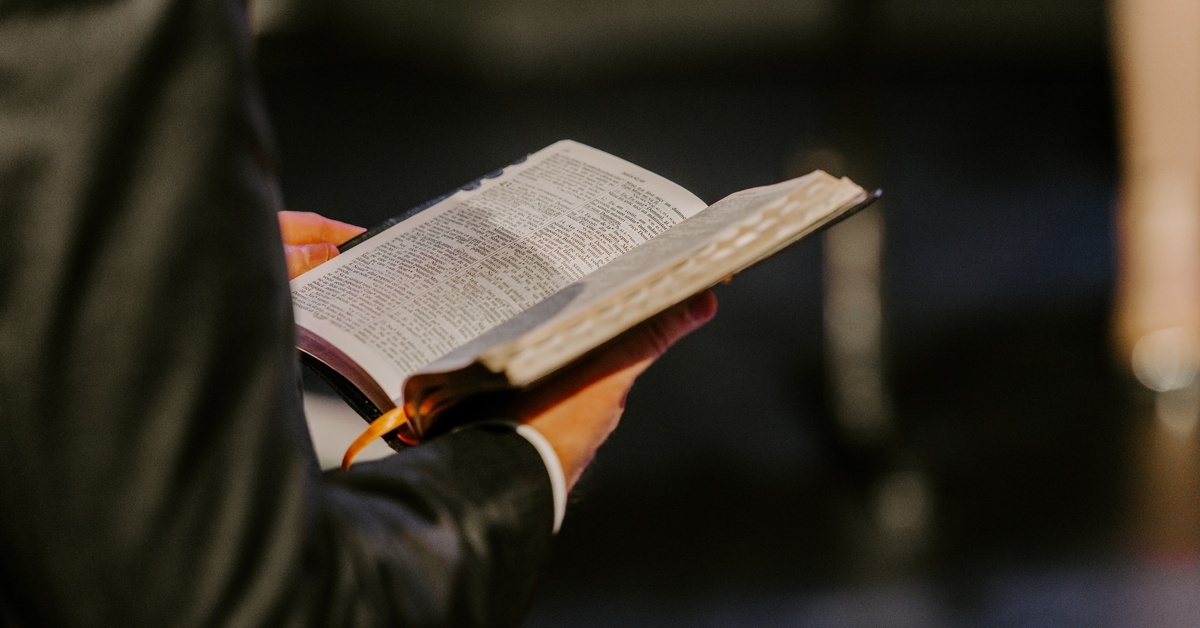 Tips for Choosing the Right Bible for Preaching A standing man in a suit holds a double-column Bible open. The Bible has a yellow ribbon and a thumb index.