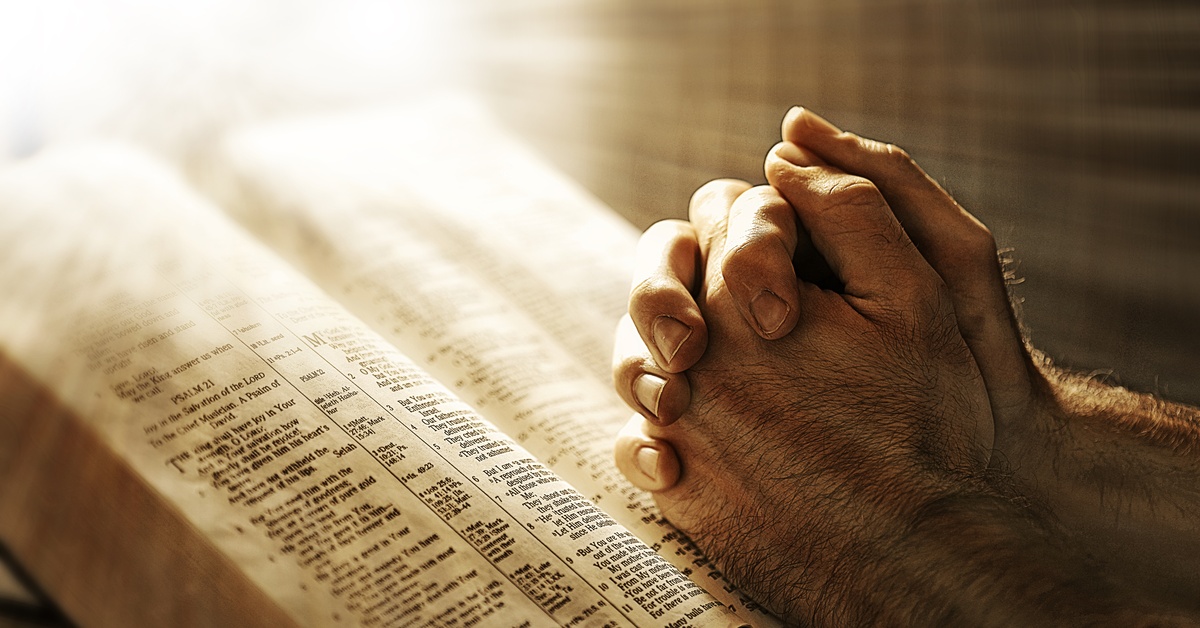 Topical vs. Expository Preaching: What’s the Difference? A person clasps their hands in prayer atop a Bible open to Psalm 21. A starburst of golden light shines from above.