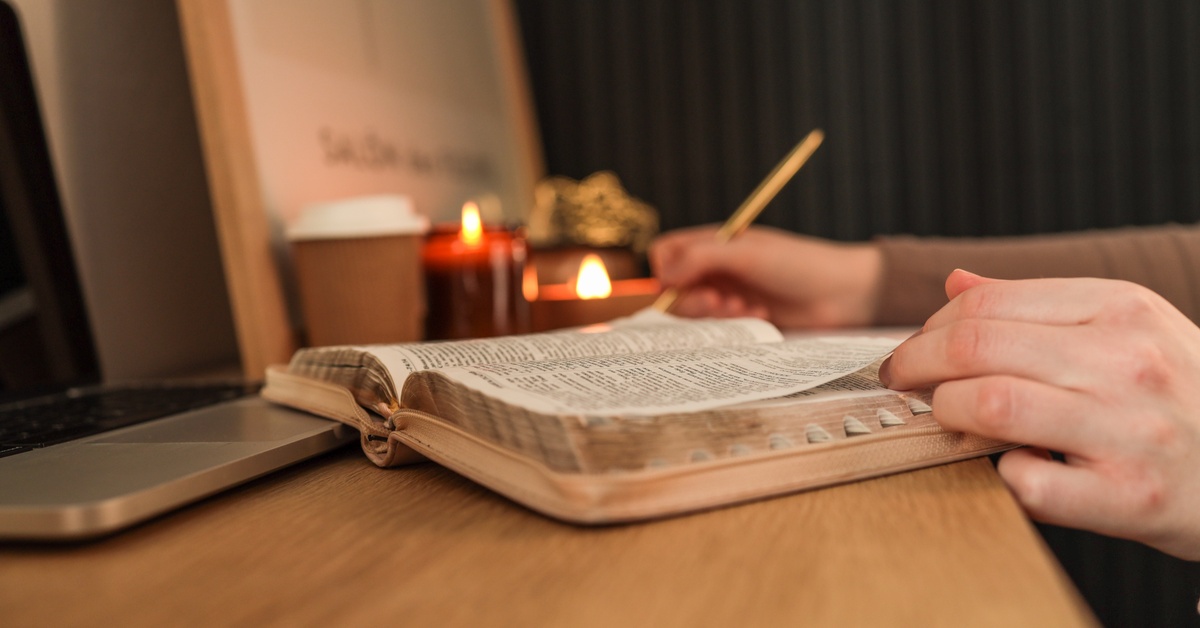 Topical vs. Expository Preaching: What’s the Difference? Close-up side view of an open Bible on a table with candles and a disposable cup. The person reading it takes notes.