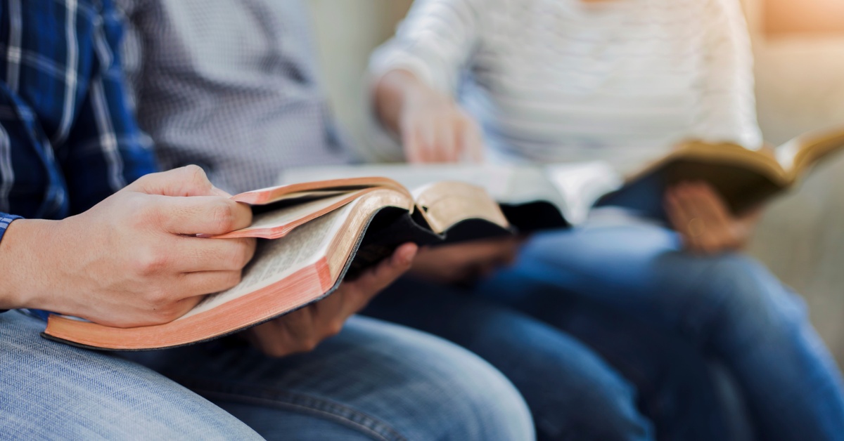 Three people sit together at Sunday School with their Bibles in their laps. One person points in another person's book.