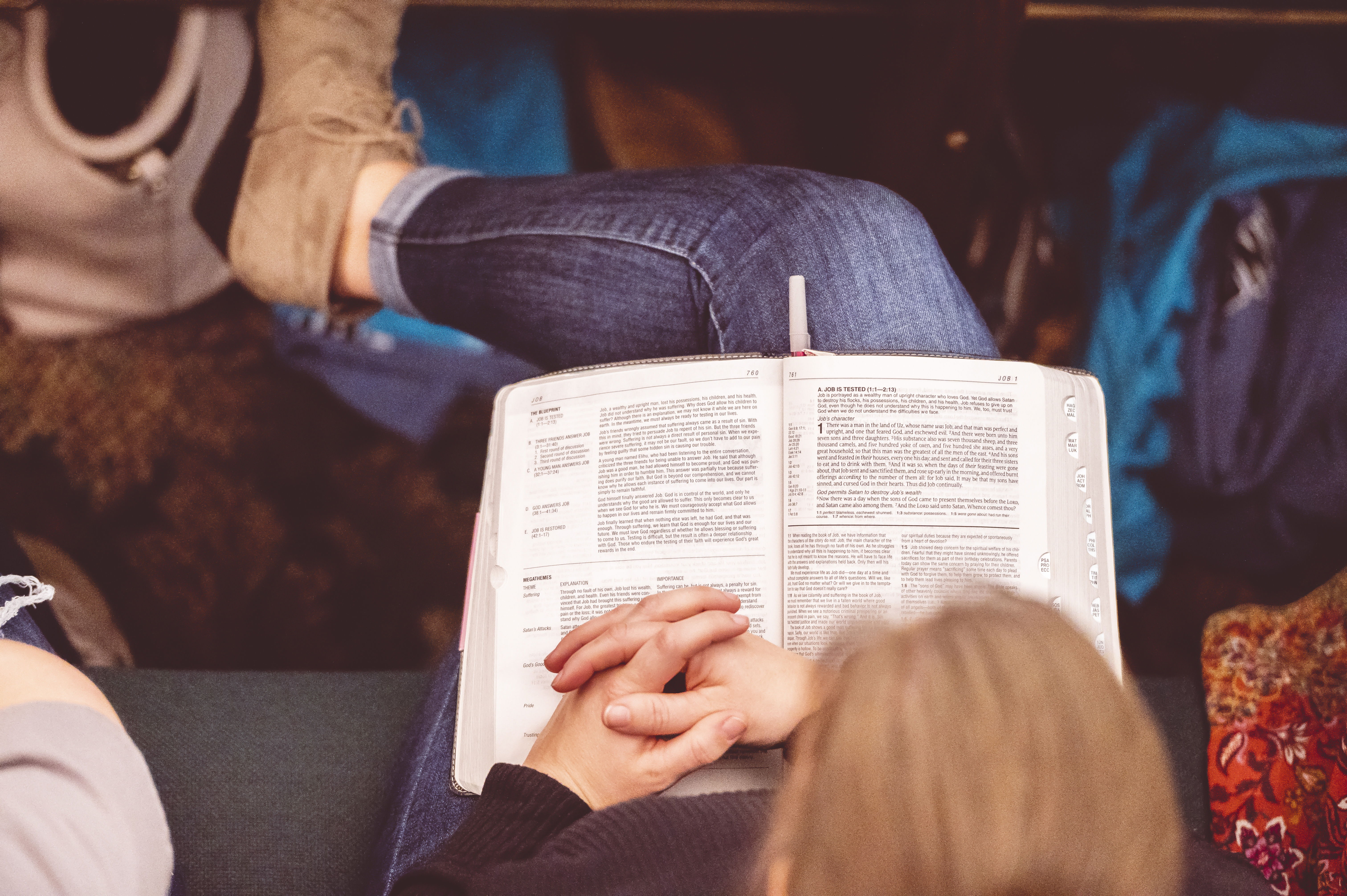 Overhead view of a woman sitting between two people. She rests her clasped hands on the Bible open on her lap.