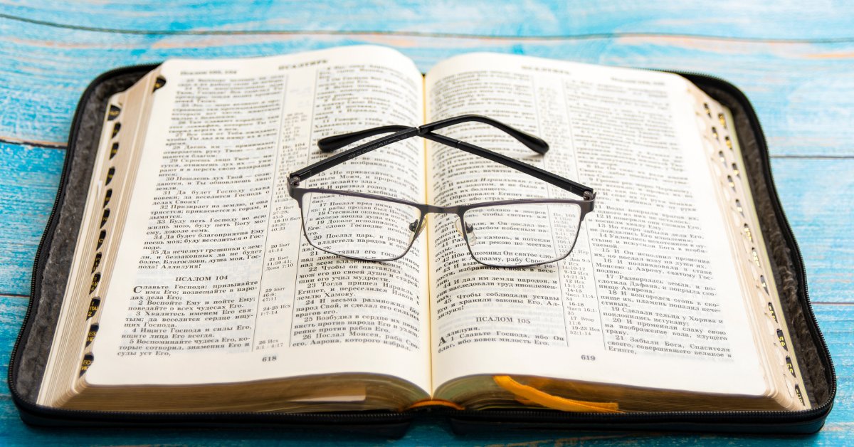 What Does It Mean To Have a Biblical Worldview? An open Bible rests on a bright blue wooden surface. A pair of black-framed eyeglasses lies across the printed pages.
