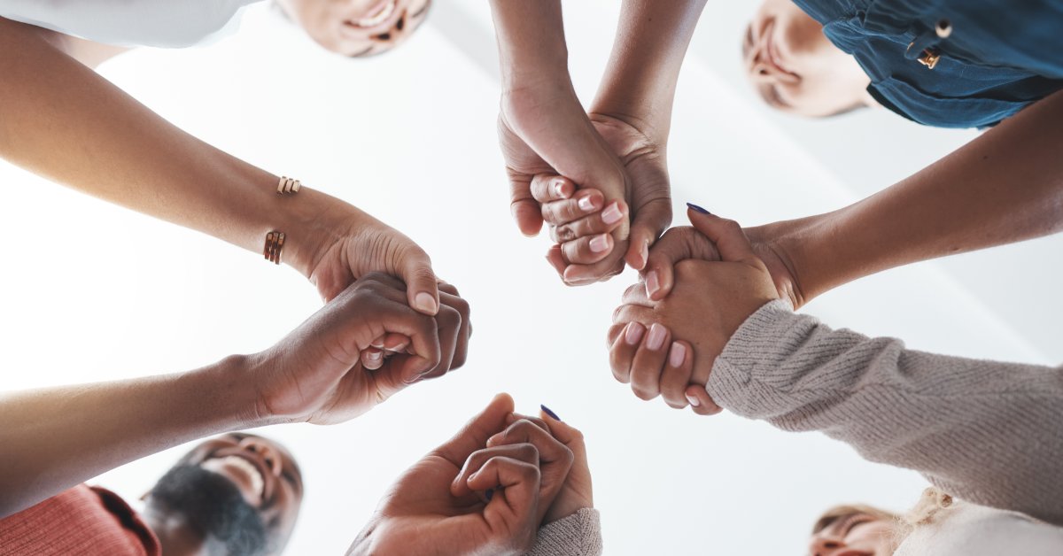 Why Community Is an Important Part of Christianity Upward view of people holding hands in a circle. Their smiling faces appear around the edges against a white background.