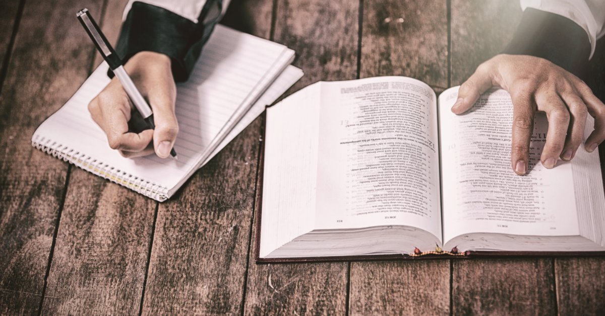 Tips for Going Beyond the Surface When Reading the Bible A person points to a Bible verse with their left hand. They hold a pen over a notebook with their right hand.