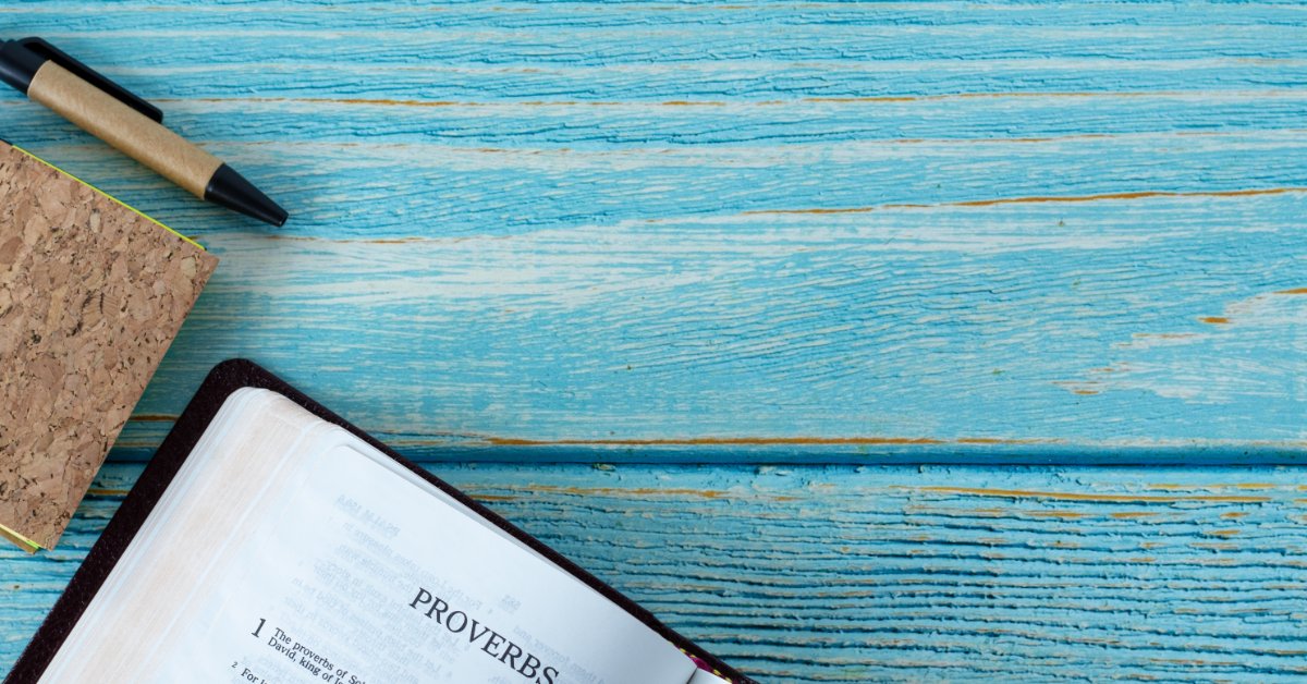 What the KJV Bible Says About Wisdom and Discernment A Bible open to Proverbs rests on a weathered turquoise wooden table. A pen and cork-covered notebook sit nearby.
